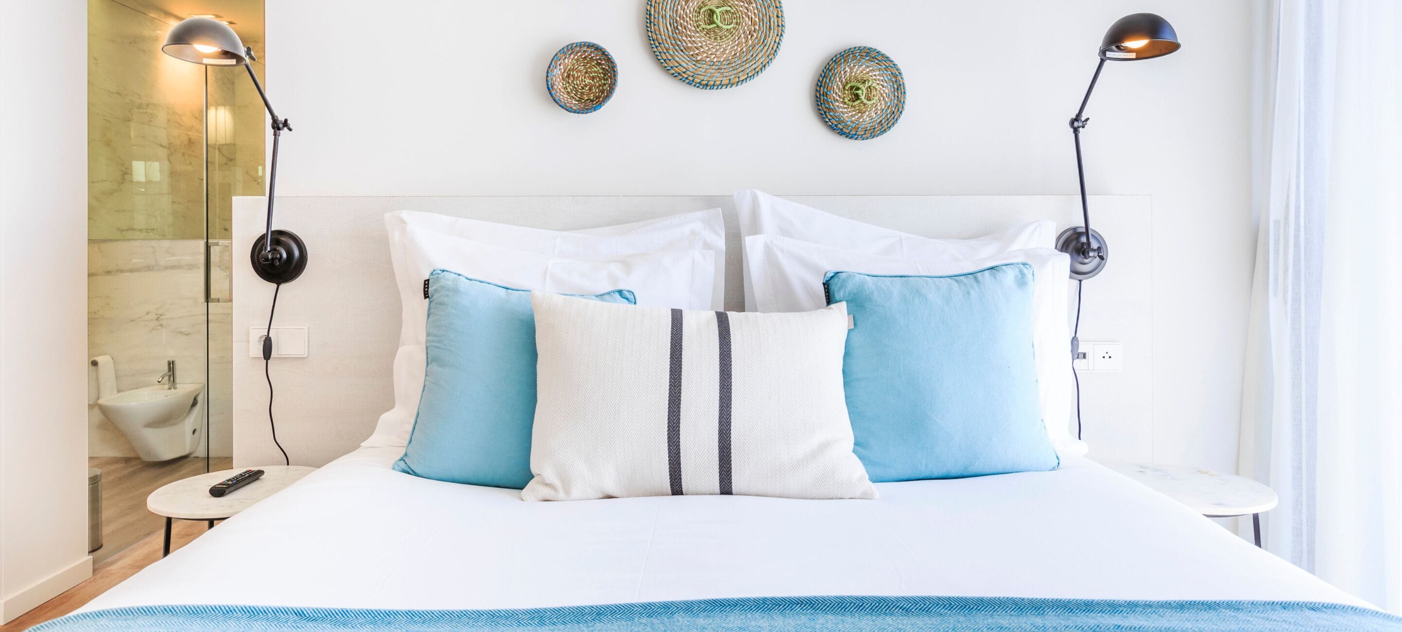 A neatly made bed with white and blue bedding, two bedside lamps, and a small table with a remote control.