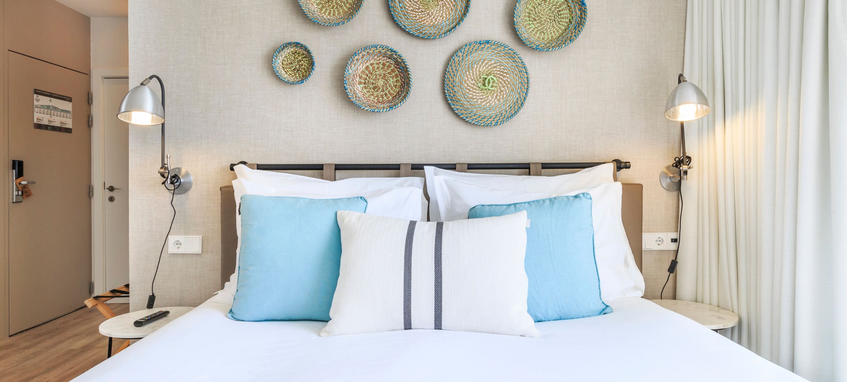 Habitación de hotel con una cama, dos lámparas de noche, una mesita de noche, un enchufe en la pared y decoración de arte tejido en la pared.