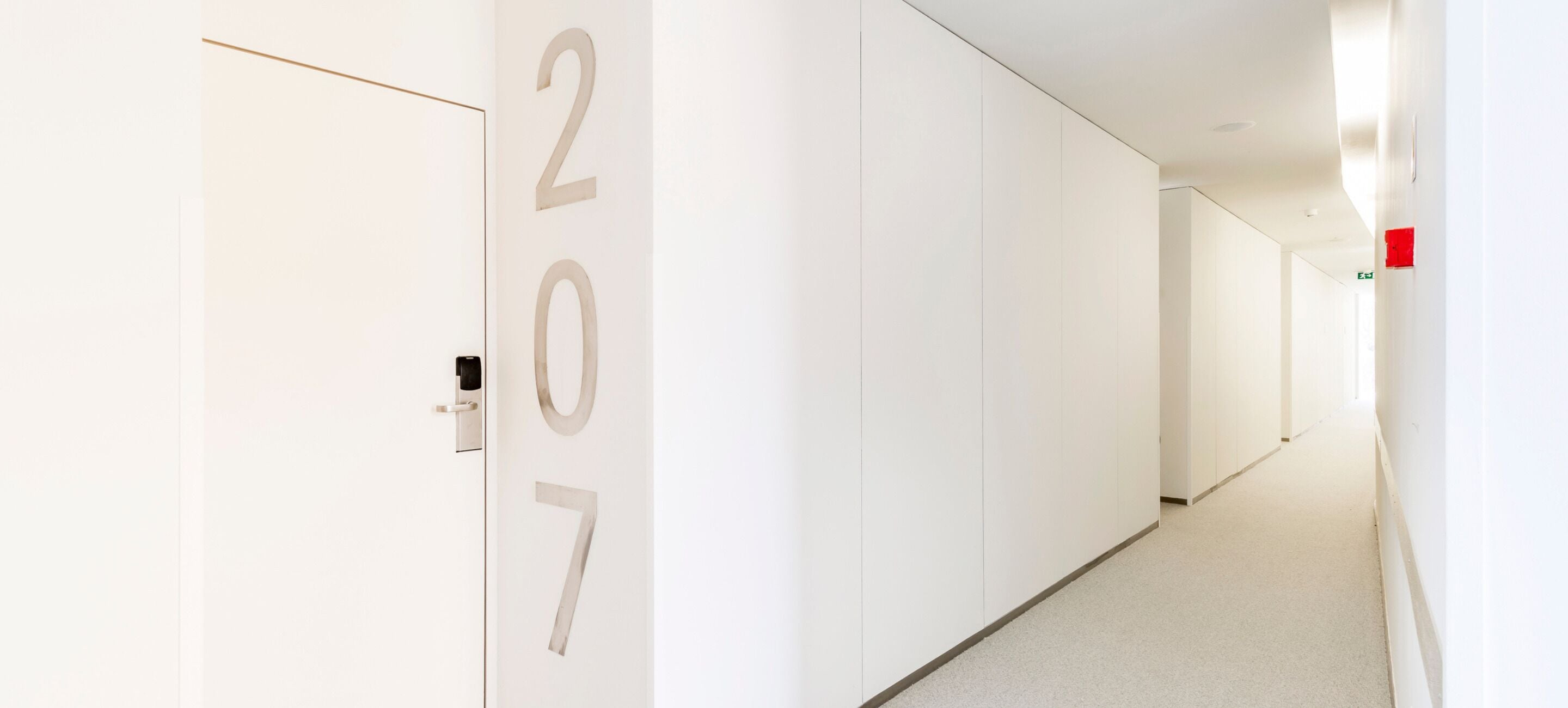A hallway with white walls and doors, featuring the numbers 207 on the left wall.