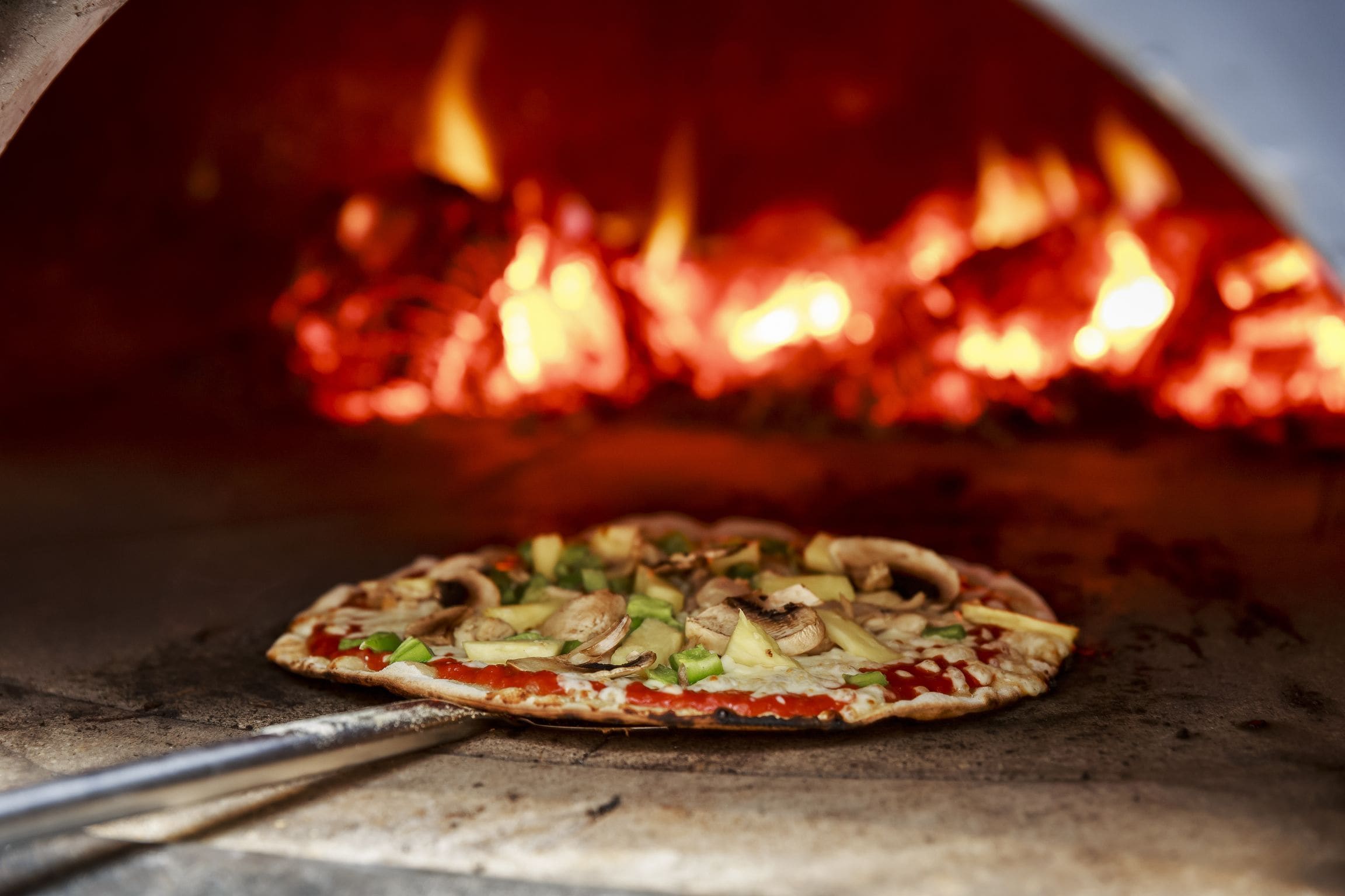 Pizza dentro de um forno a lenha, com chamas visíveis.