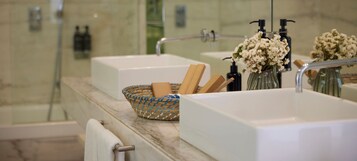 Un baño con encimera de mármol, dos lavamanos, ducha y toallero.