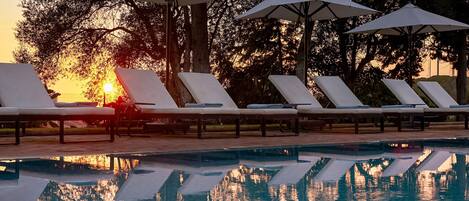 A poolside area with lounge chairs and umbrellas, reflecting the sunset.