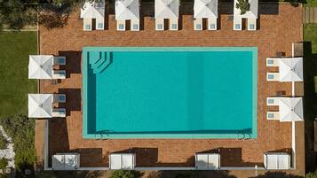 Vista aérea de una piscina rectangular con solárium azulejado, rodeada de sombrillas blancas y sillas de descanso.