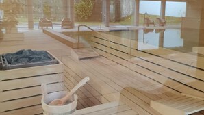 A spacious room with wooden flooring, a sauna area with benches, a glass-enclosed window, and a sauna with a stone floor. - Hotel Do Parque - Congress & SPA (Sao Pedro do Sul)