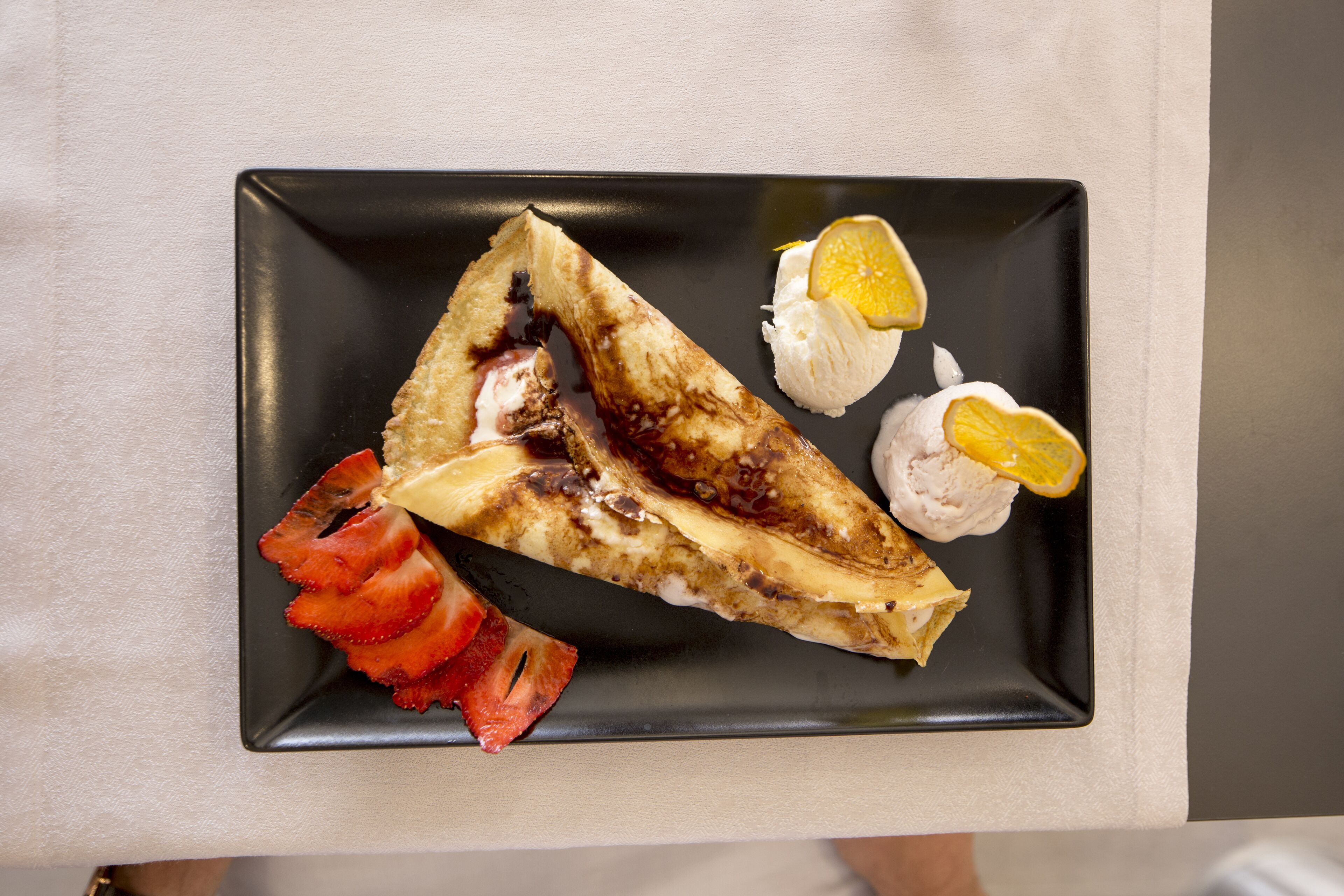 A black rectangular plate with a crepe, strawberries, and lemon slices.
