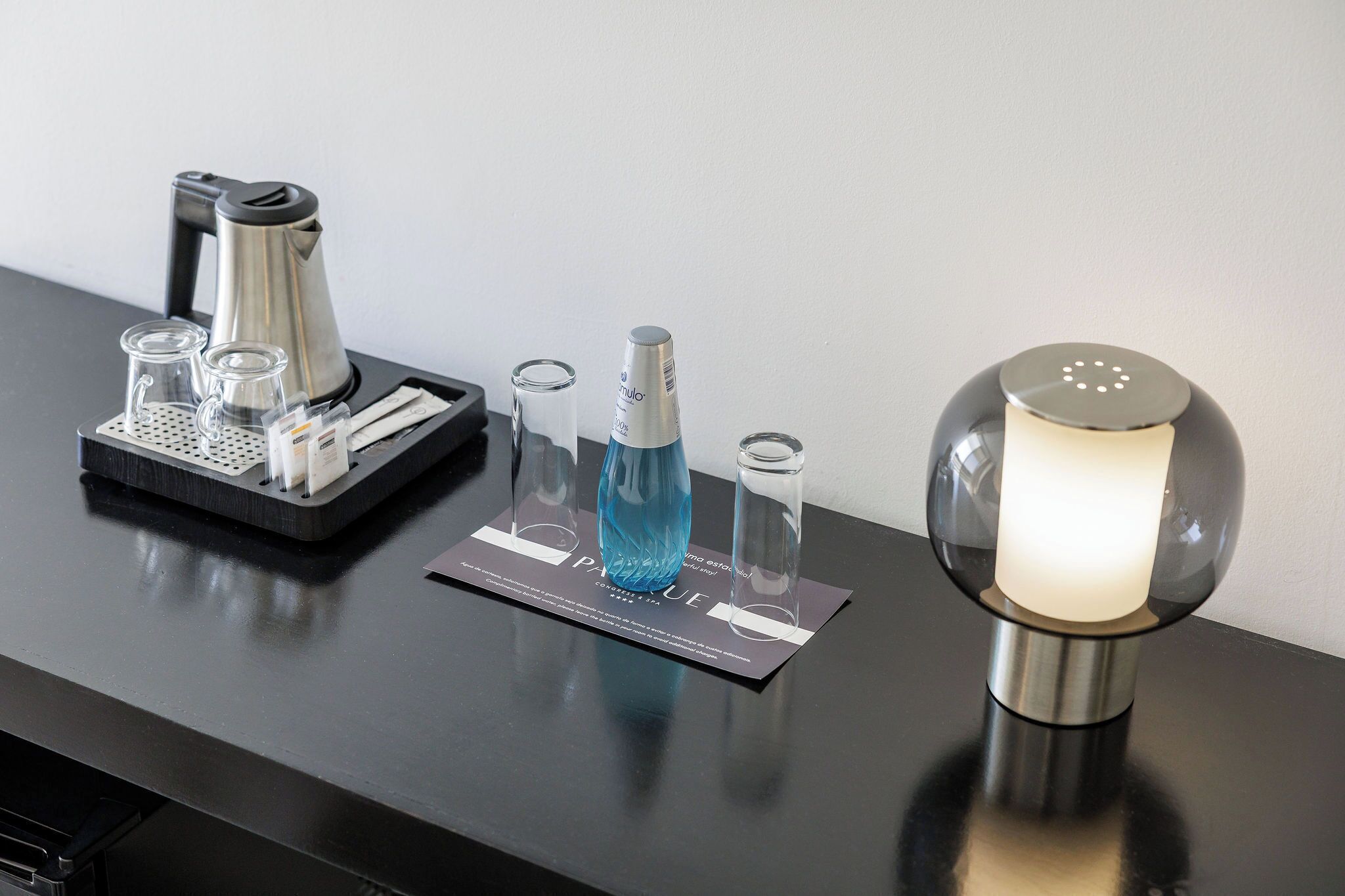 A table with a coffee maker, a bottle of blue liquid, a candle, and a card with text.