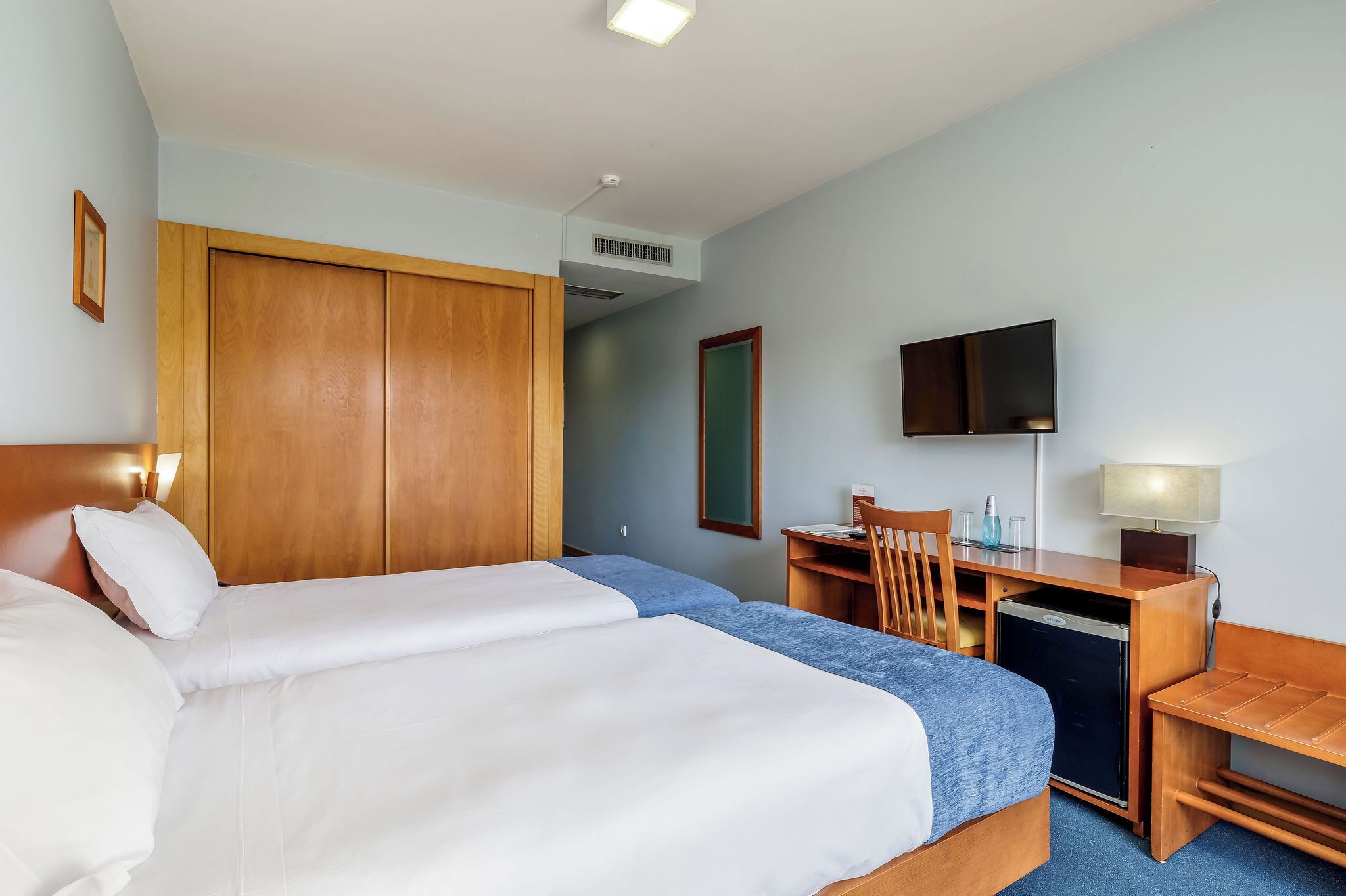 A hotel room with a large bed, a desk, a chair, a television, and a wardrobe.