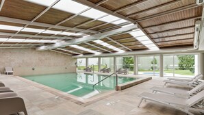 An indoor swimming pool with clear glass walls, lounge chairs, and a wooden ceiling. - Hotel Do Parque - Congress & SPA (Sao Pedro do Sul)