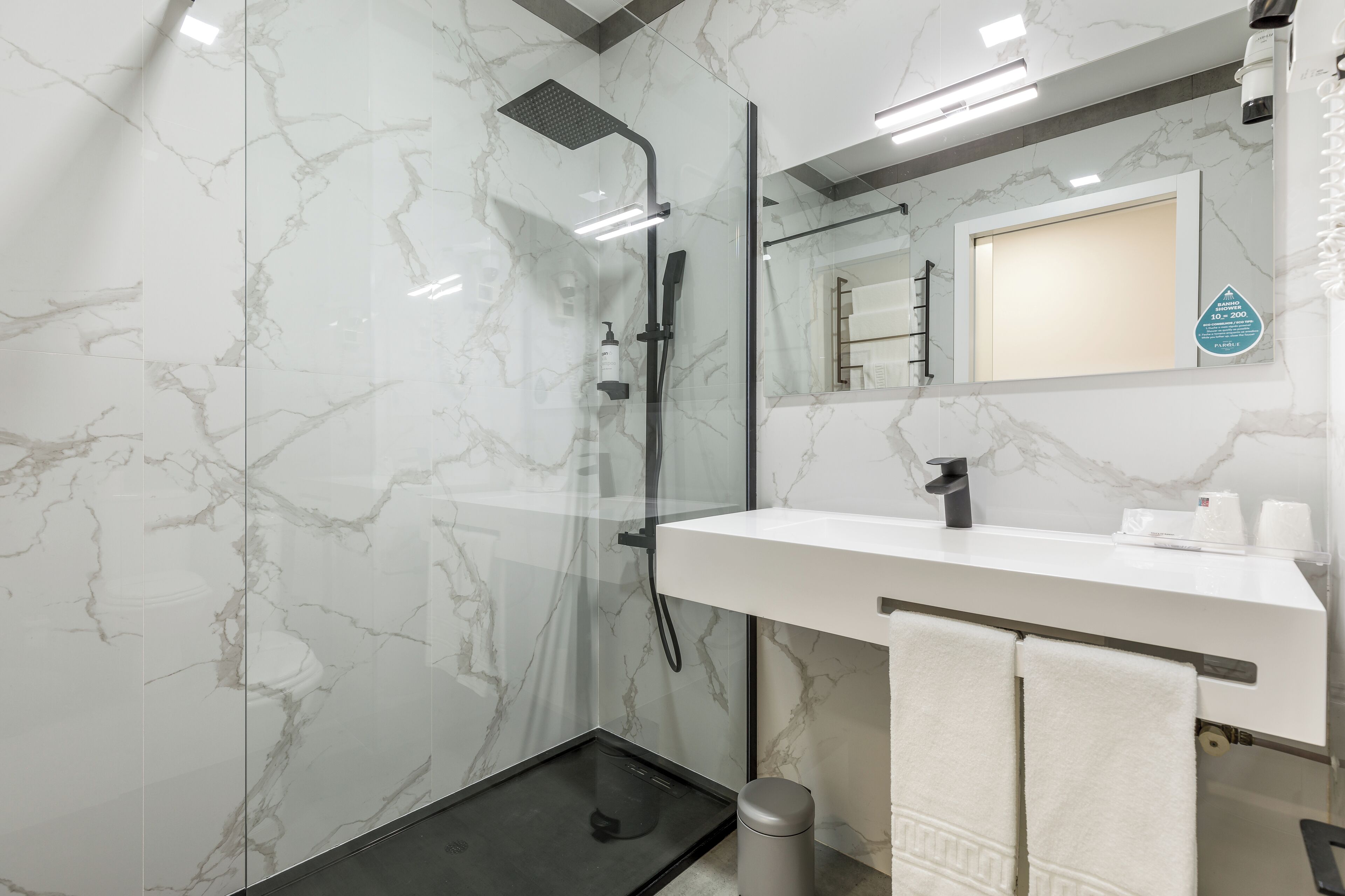 A modern bathroom with a glass-enclosed shower, a white marble backsplash, and a large mirror above a white sink.