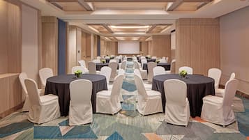 A conference room with round tables, white chairs, and a carpeted floor.