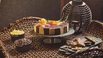 Un pastel con diseño a rayas de chocolate y rojo, rodeado de trozos de chocolate y un candelabro decorativo.