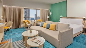 Une chambre d’hôtel avec un lit, un canapé, deux fauteuils, une petite table et une fenêtre avec des rideaux.