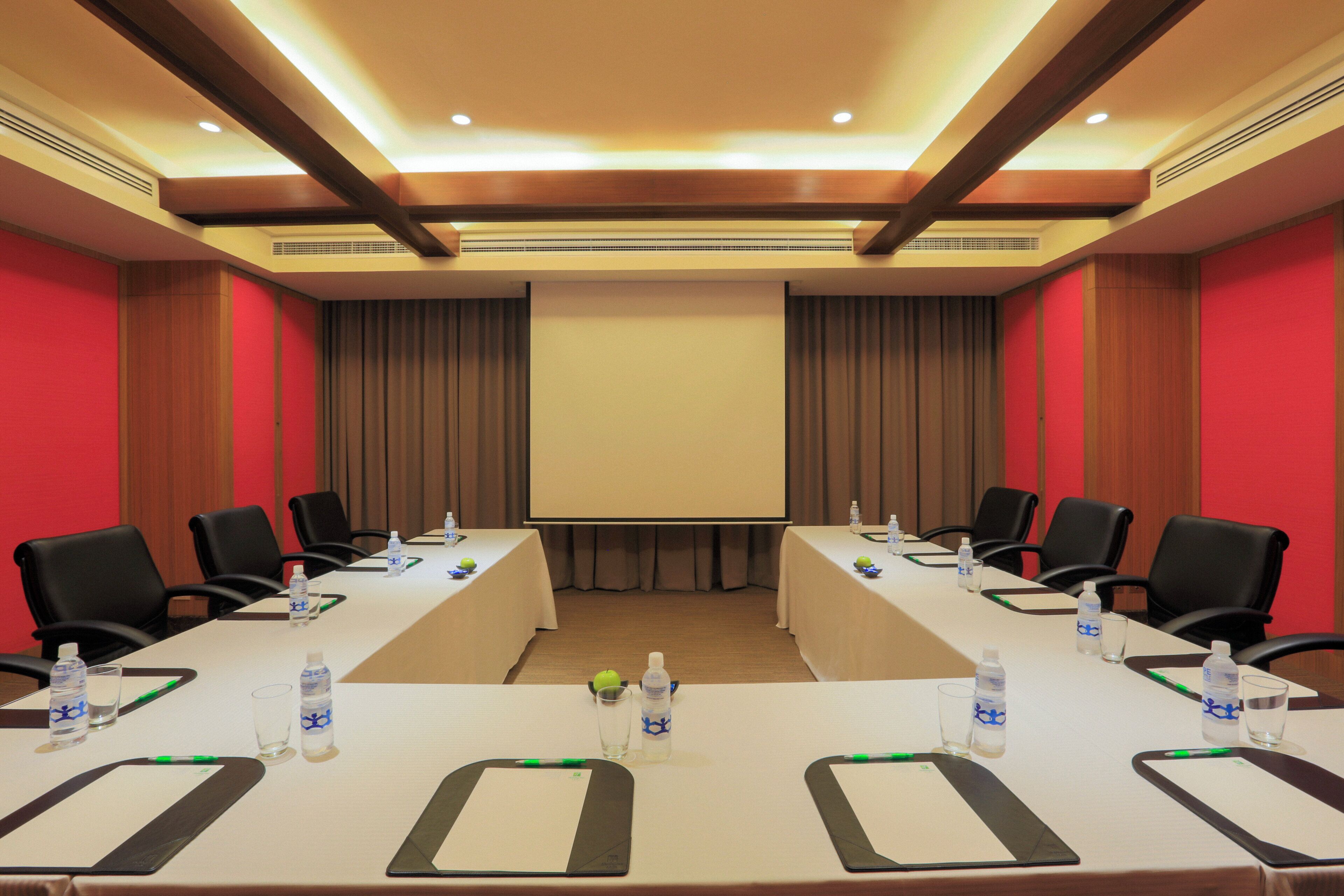 A conference room with a long table, chairs, a projector screen, and water bottles.