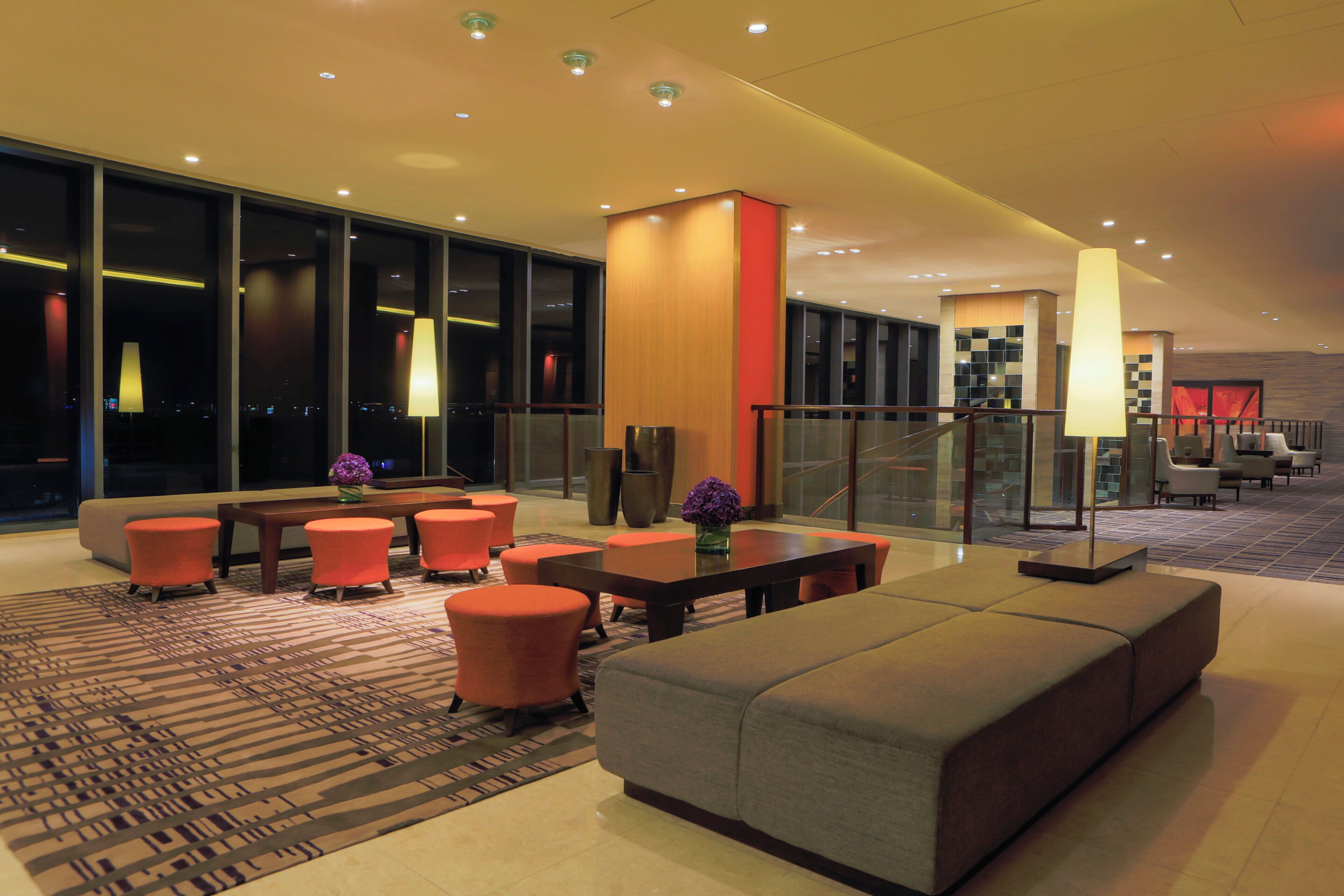 Eine moderne Hotelhalle mit Sitzgelegenheit, einer Rezeption und Blick auf die Stadt durch große Fenster.