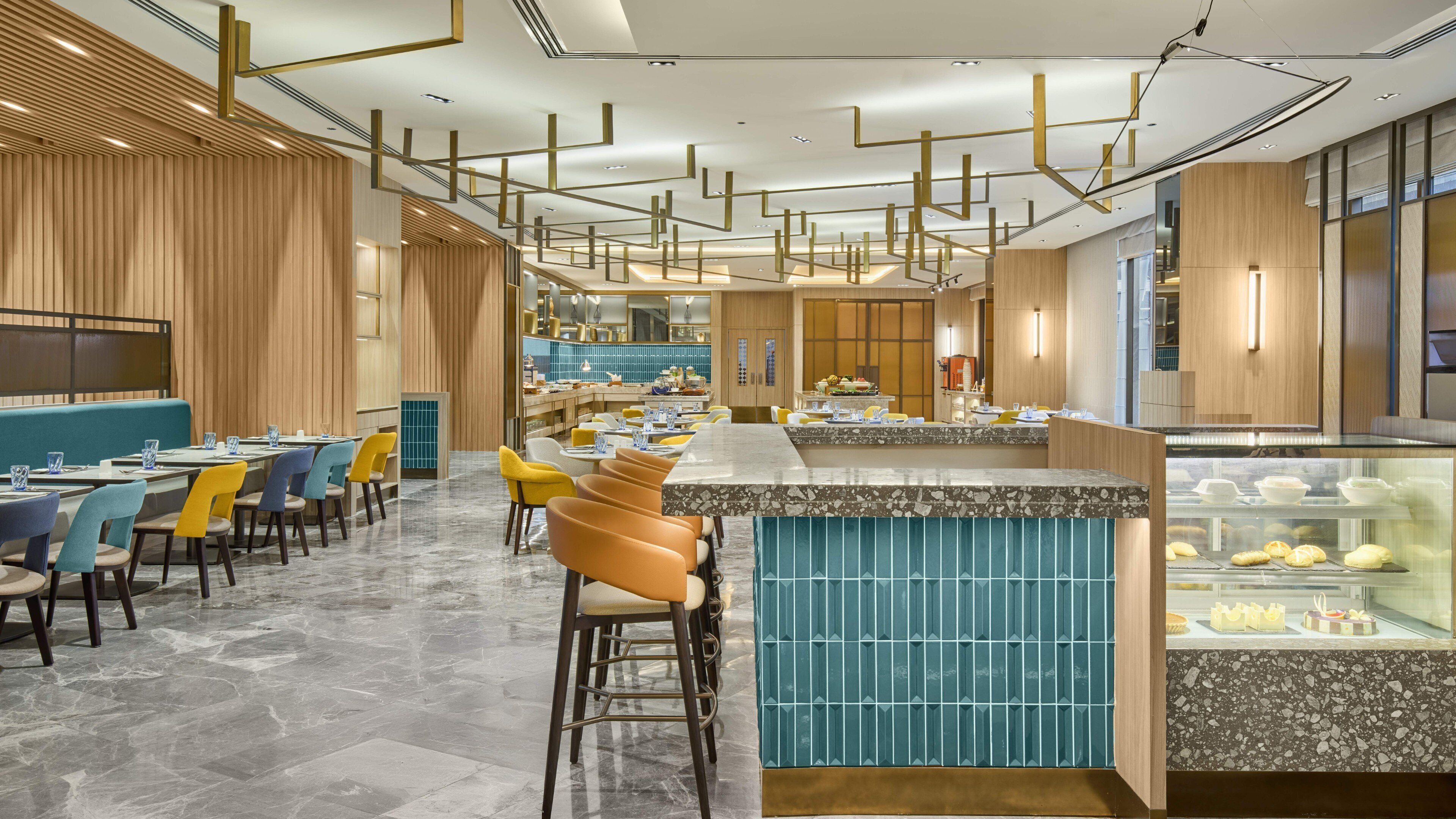 A modern restaurant with a central bar, seating areas, and a display case with pastries.