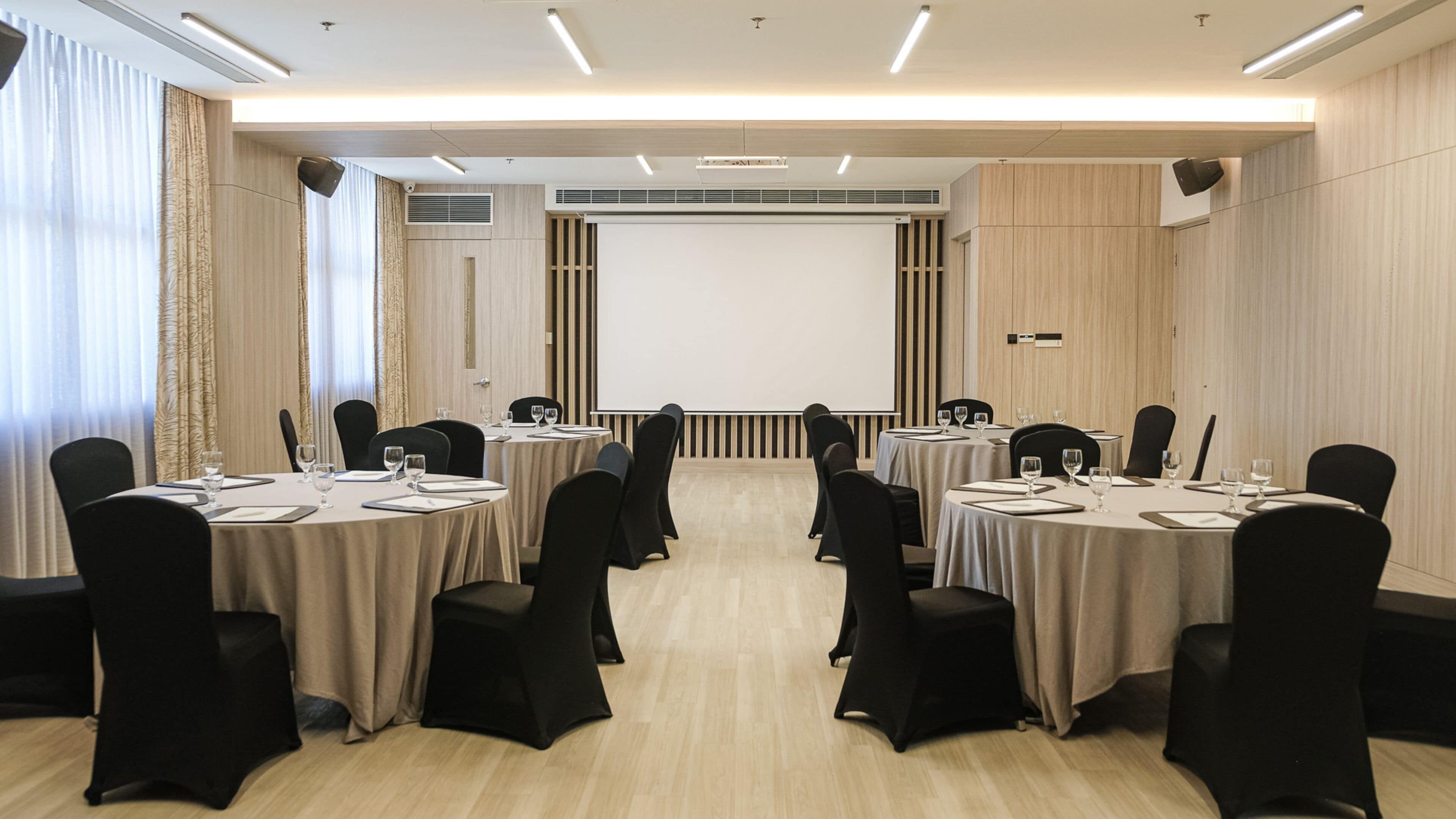 A conference room with round tables, black chairs, and a large screen at the front.