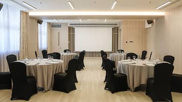 A conference room with round tables, black chairs, and a large screen at the front.