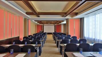 A conference room with rows of tables and chairs, a projector screen at the front, and large windows on one side.