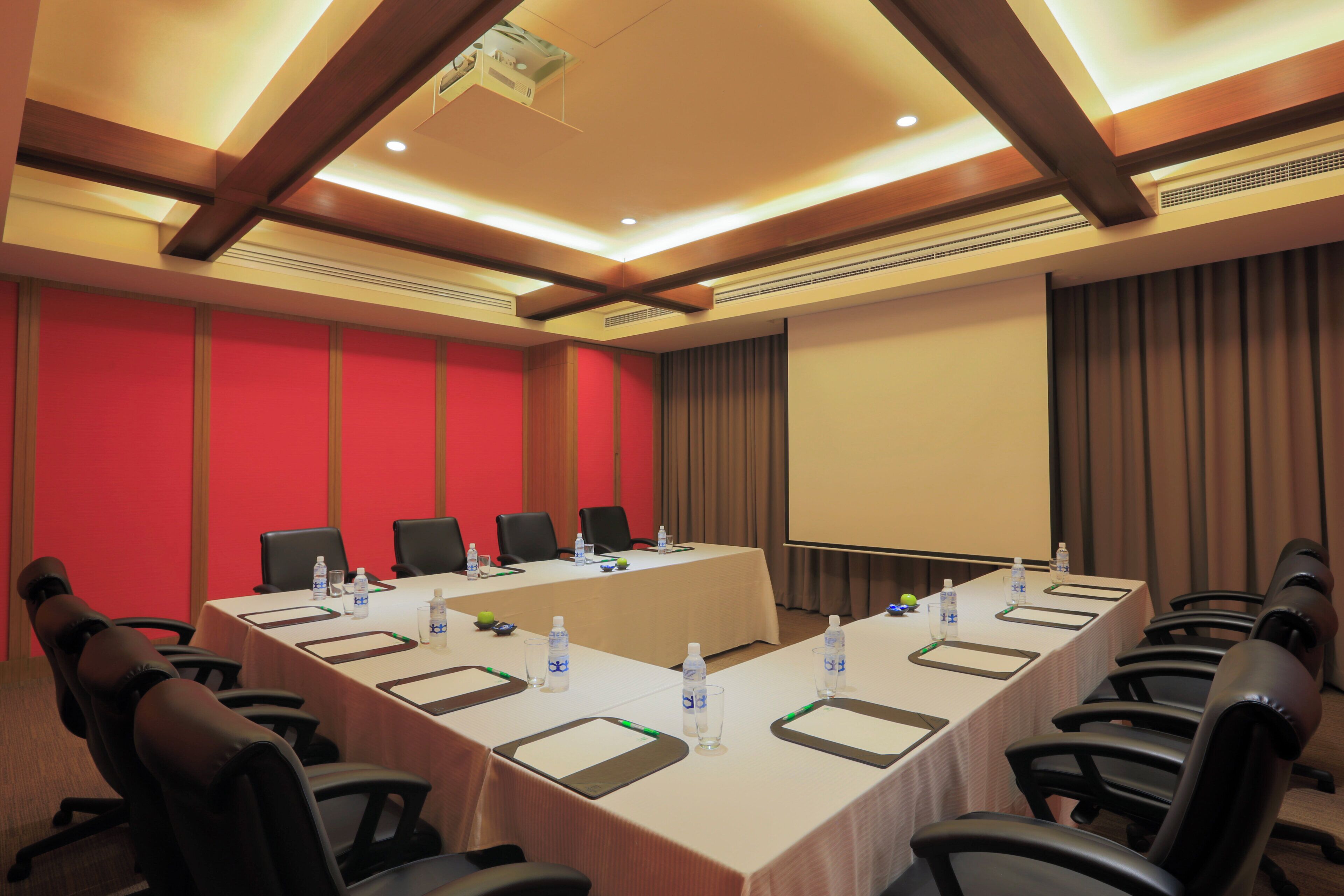 A conference room with a long table, chairs, a projector, and a screen.
