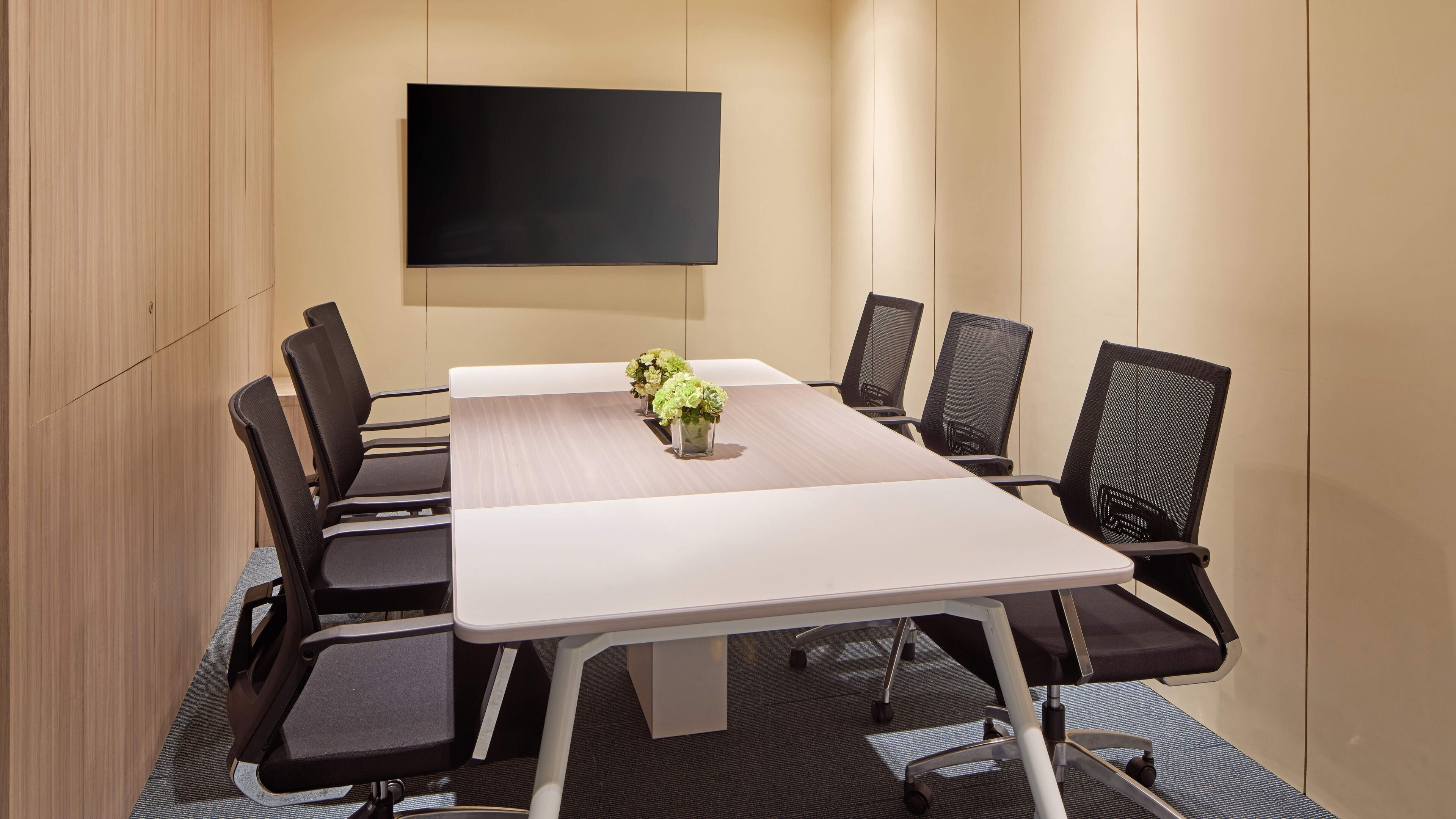 A conference room with a long table, black chairs, a flat-screen TV, and a vase with flowers.