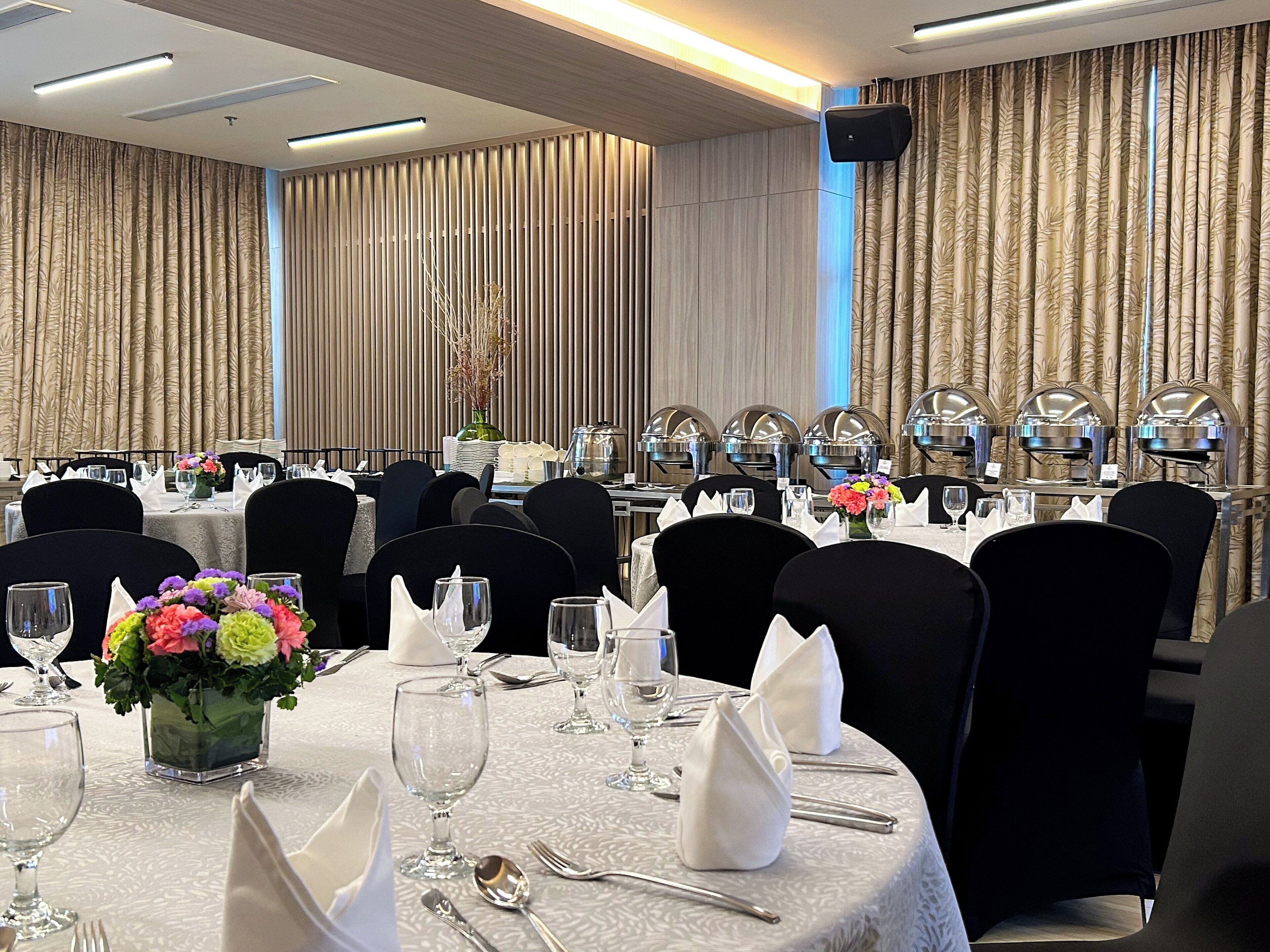 A banquet hall with round tables set for dining, featuring white tablecloths, black chairs, and floral centerpieces.