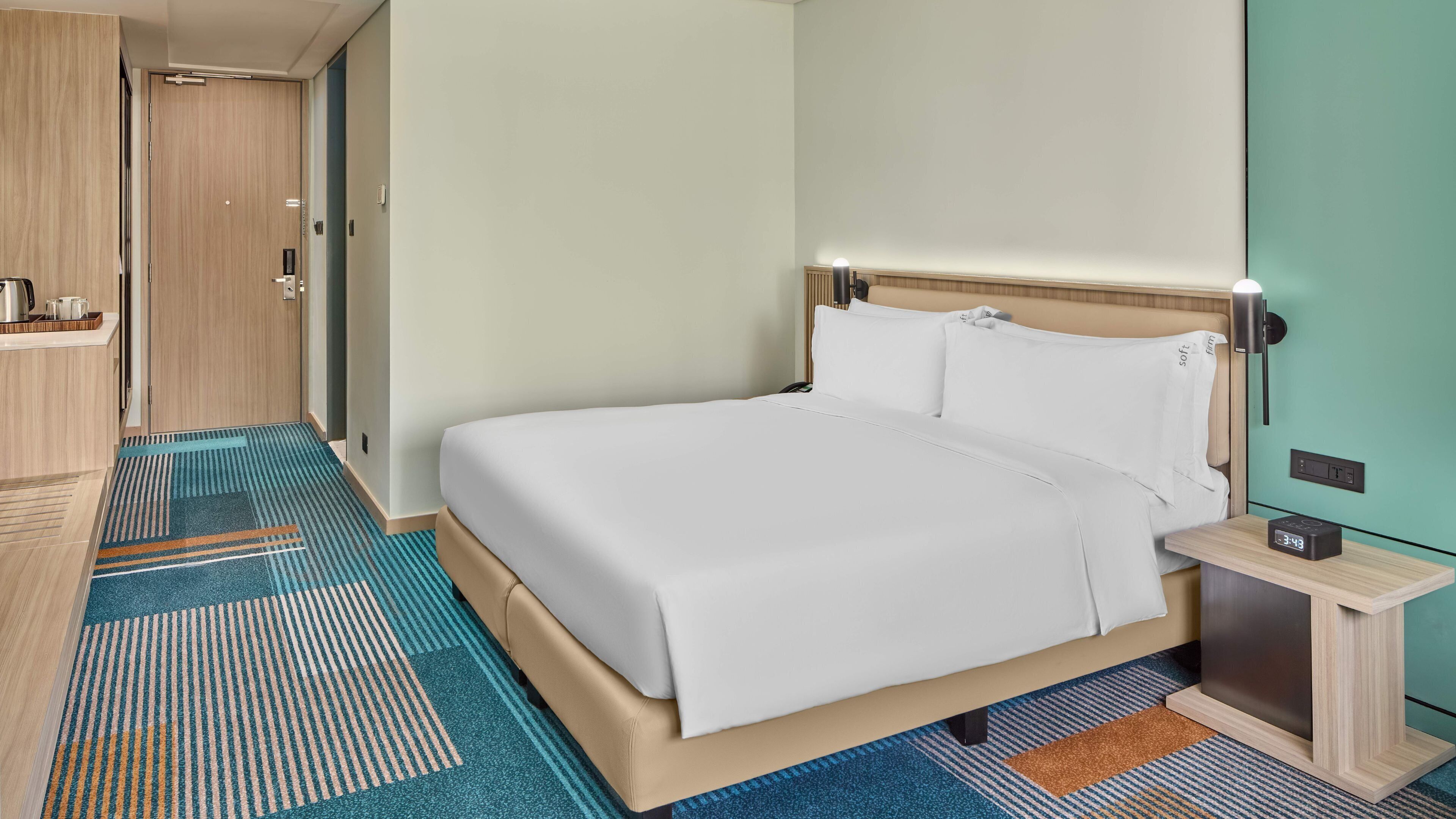 A hotel room with a bed, bedside table, and a nightstand with a clock.