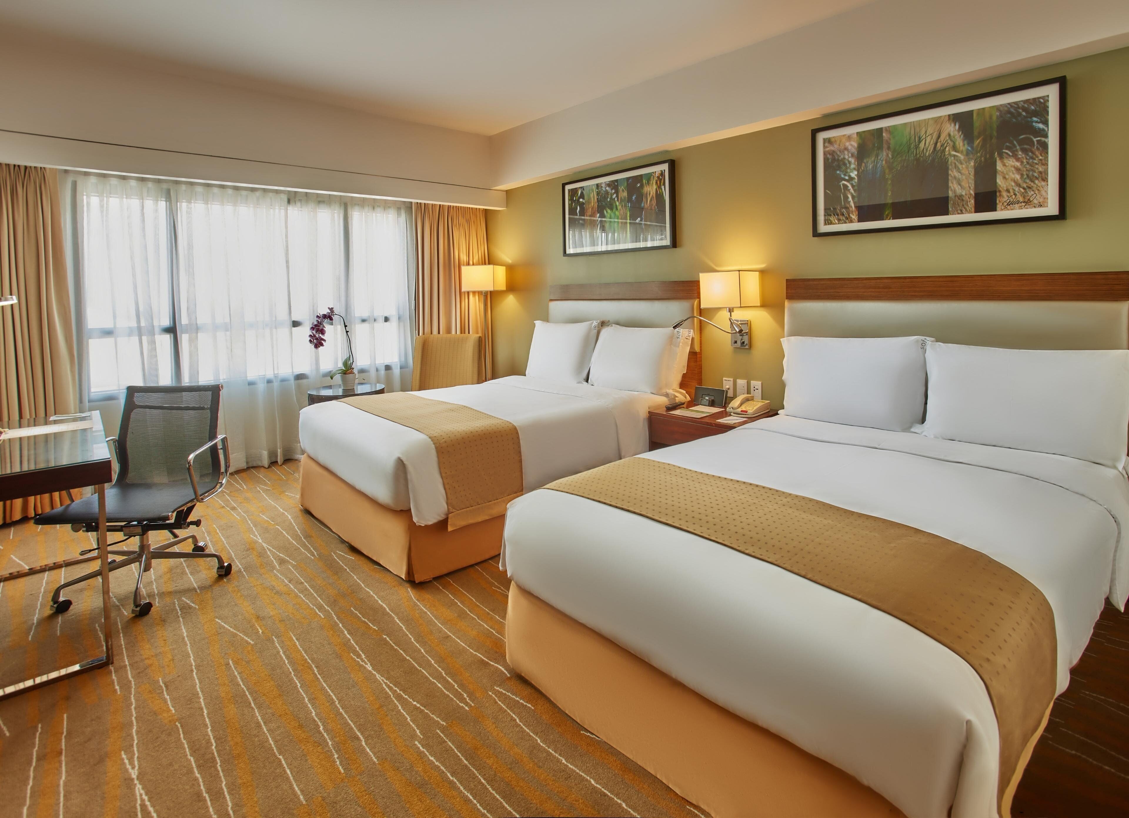A hotel room with two beds, a desk, a chair, and a window with curtains.