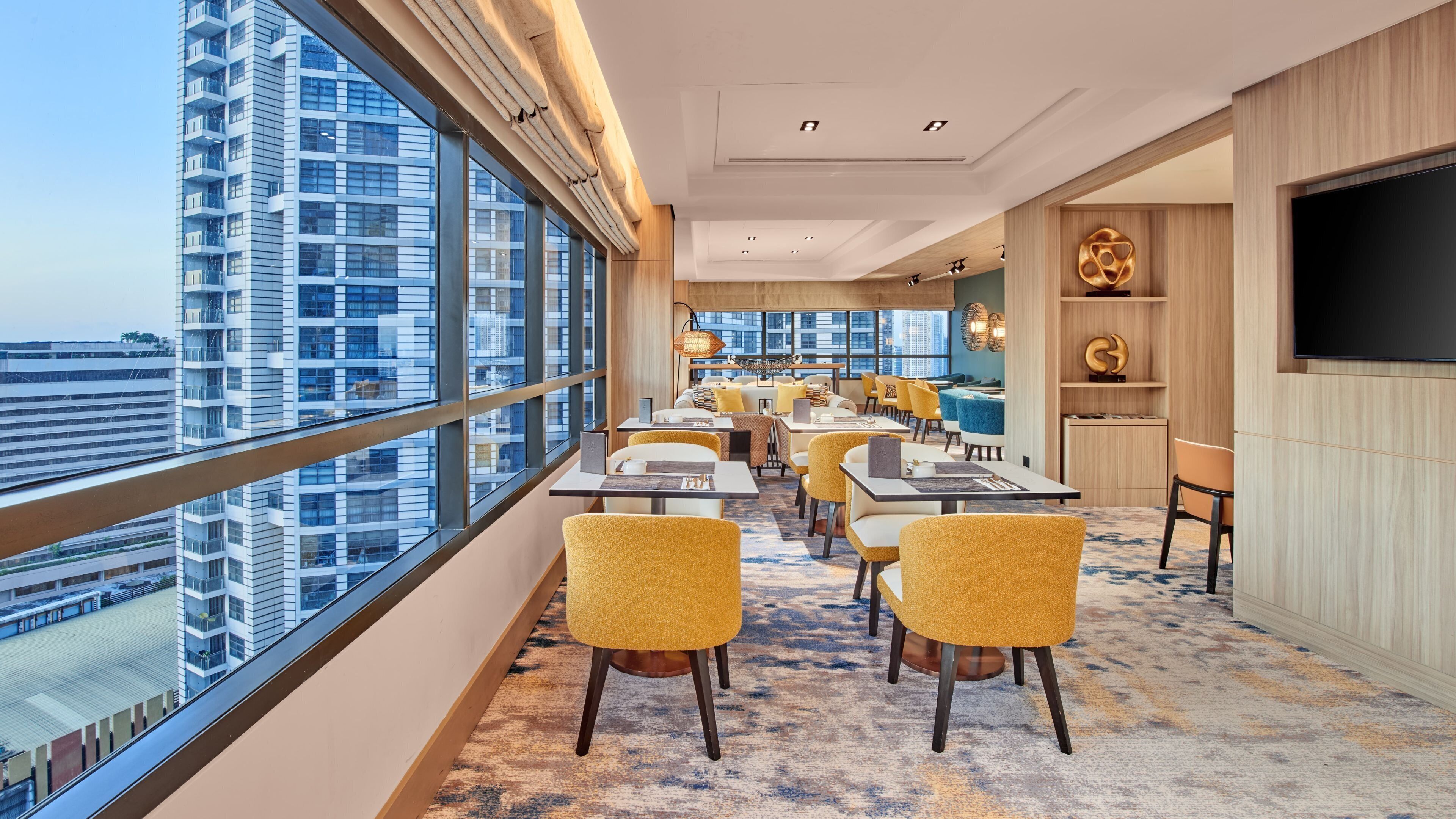 A modern dining area with high ceilings, large windows, and a city view.