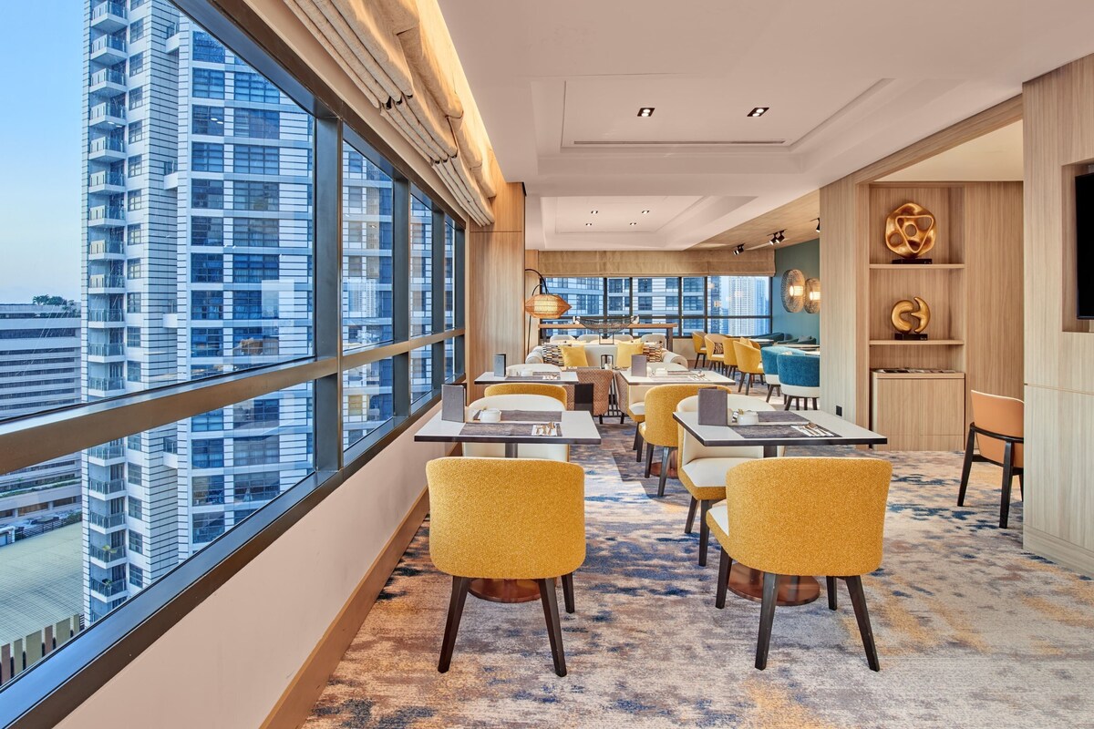 A modern dining area with high ceilings, large windows, and a city view.