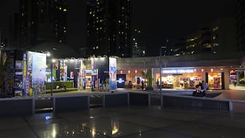 A nighttime urban plaza with a seating area and a restaurant named "Makahata Tomi-Ichi".