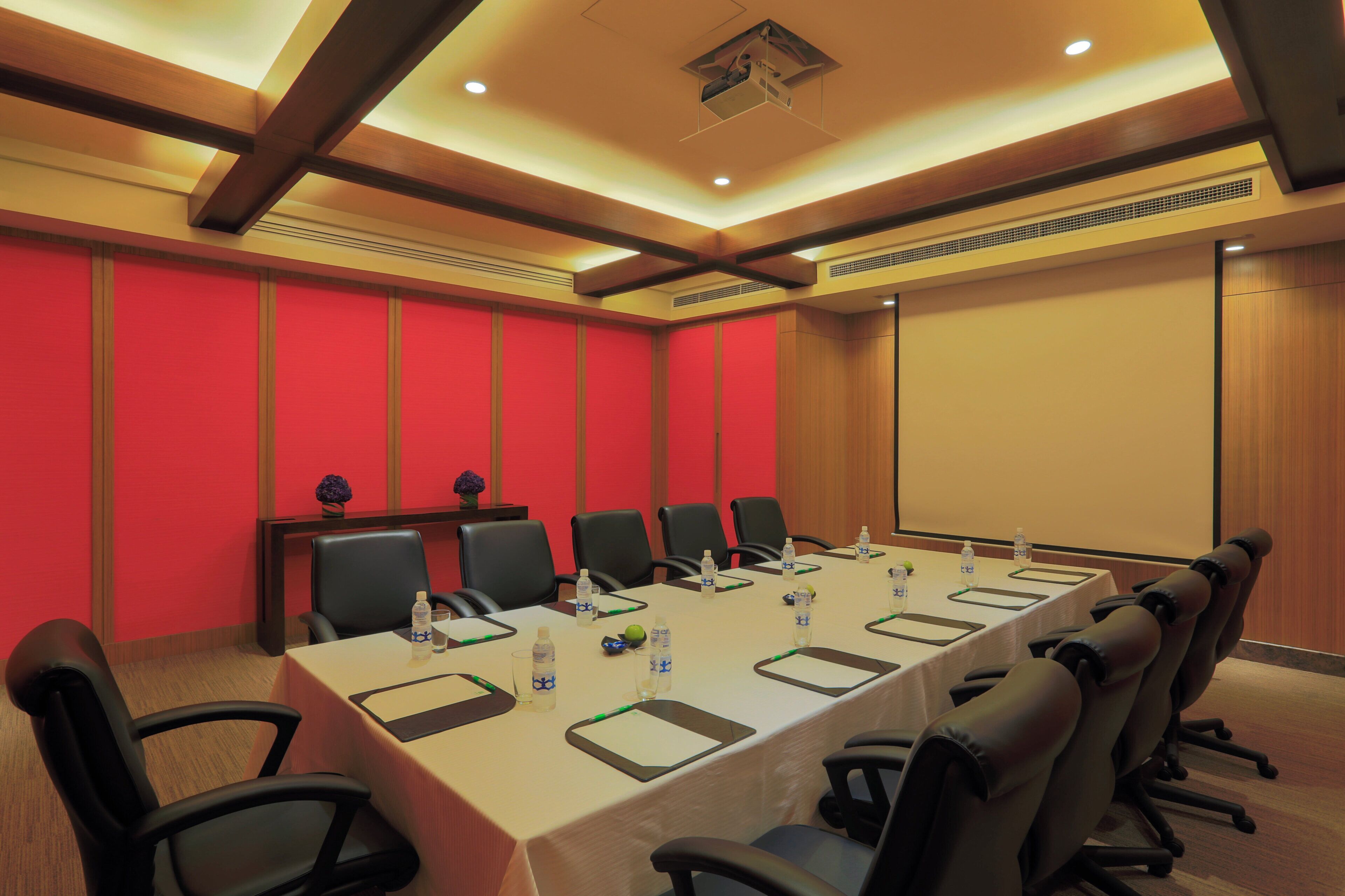 A conference room with a long table, chairs, water bottles, and a projector screen.