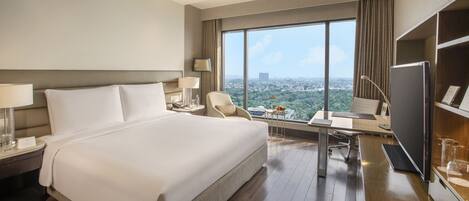 A hotel room with a large bed, a desk with a chair, a television, and a view of the city.