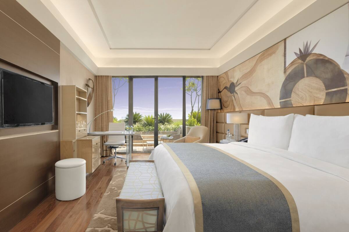 Une chambre d’hôtel avec un grand lit, une télévision, un bureau avec une chaise, une petite table et une vue sur l’extérieur.