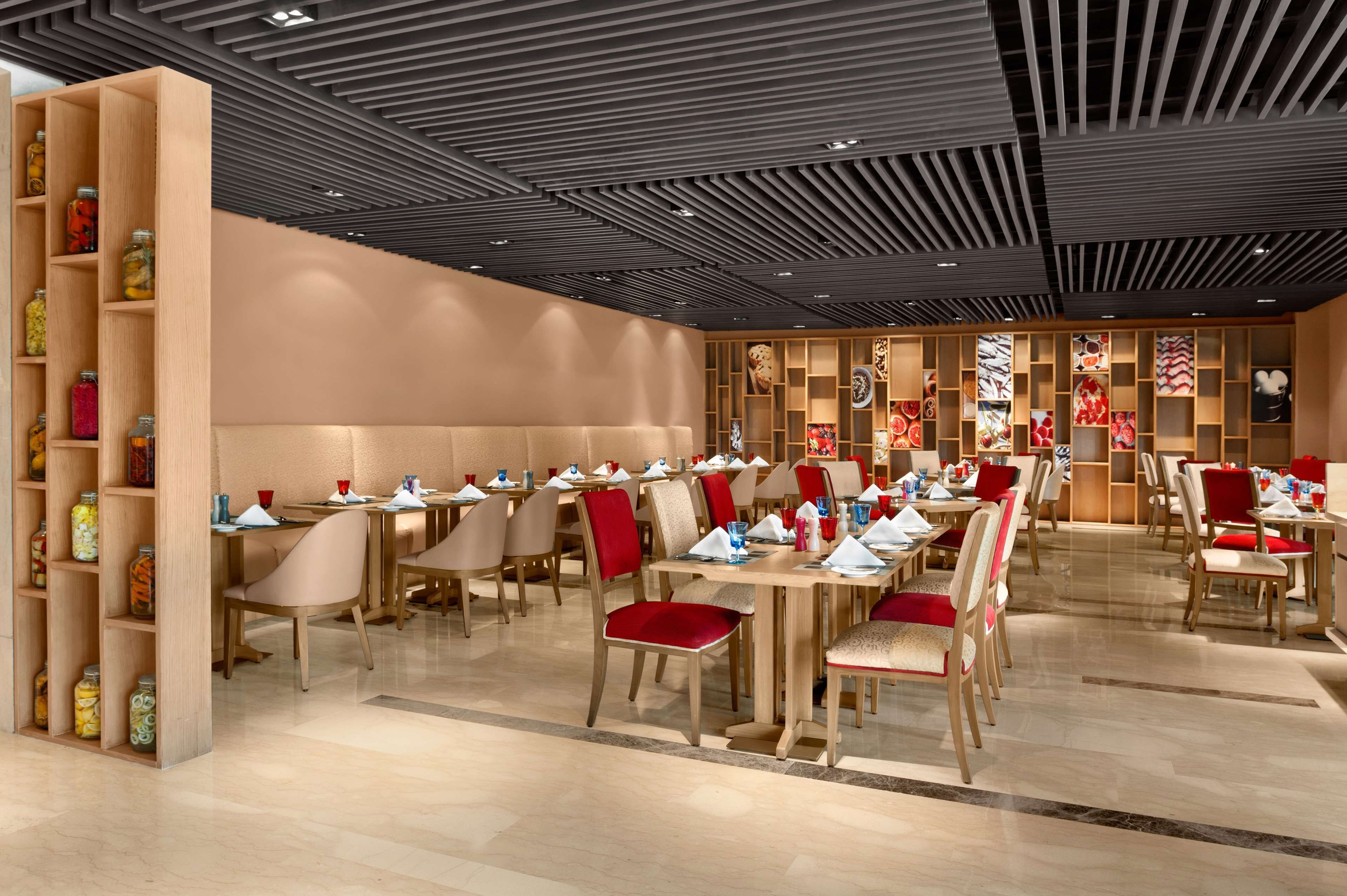 A modern restaurant with wooden tables and chairs, a patterned ceiling, and shelves with jars.