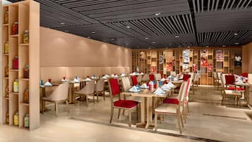 A modern restaurant with wooden tables and chairs, a patterned ceiling, and shelves with jars.