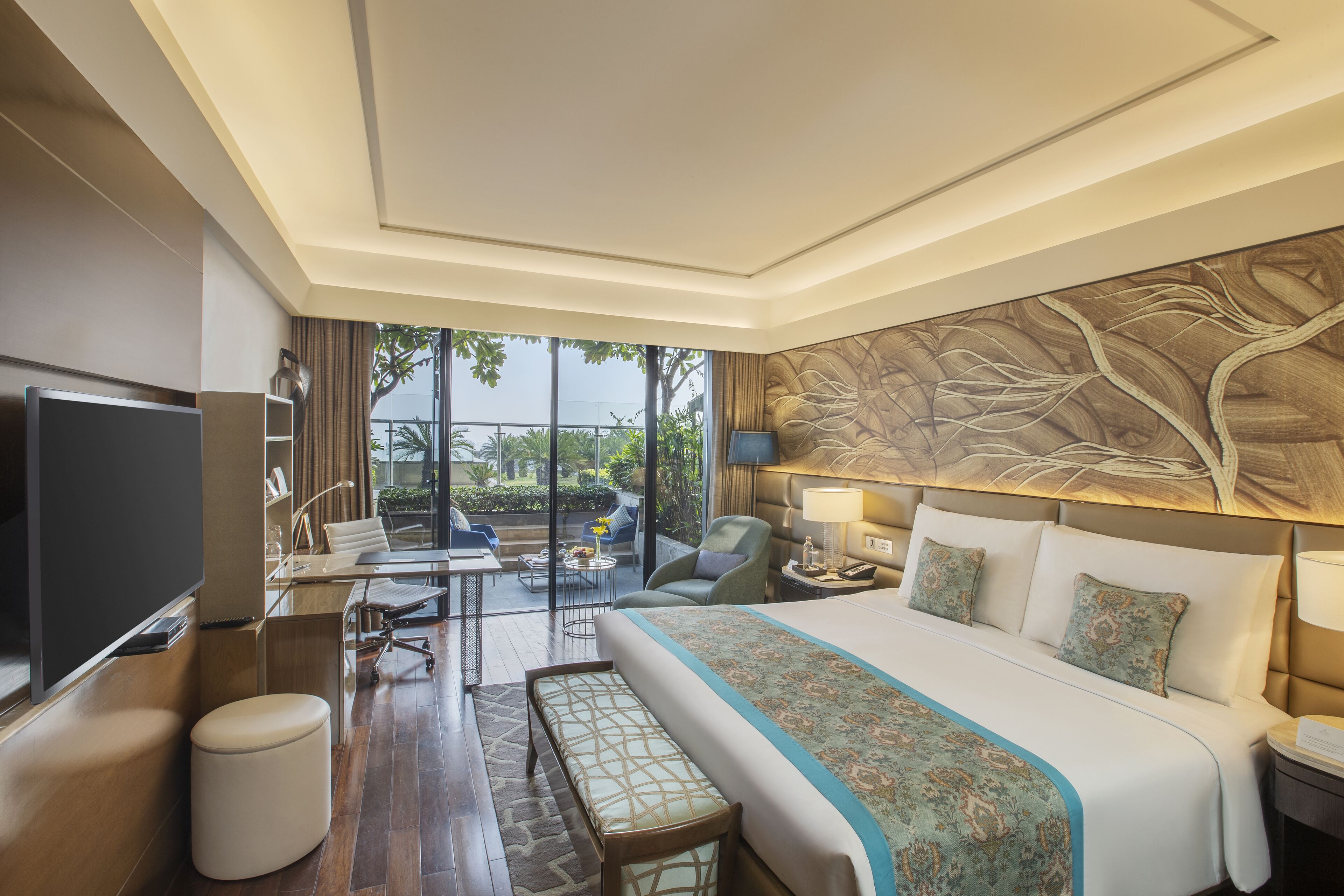 Quarto de hotel com uma cama grande, uma escrivaninha com computador, televisão e vista para o exterior.