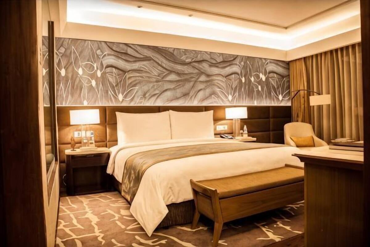 Une chambre d’hôtel avec un grand lit, des tables de chevet avec des lampes, un banc, un bureau et un mur au décor texturé.
