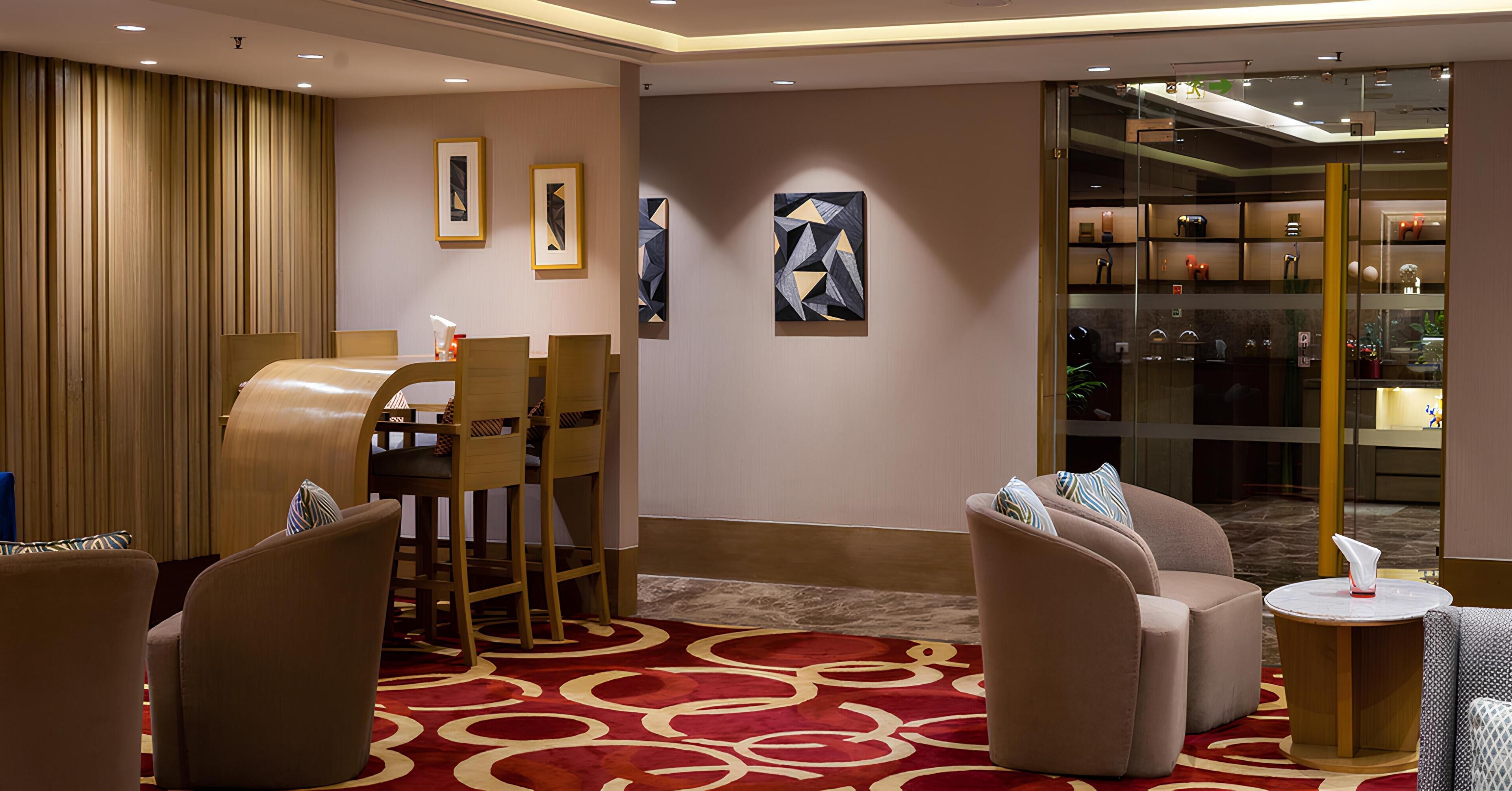 A hotel lobby with a reception desk, seating area, artwork on the walls, and a glass display case with items.
