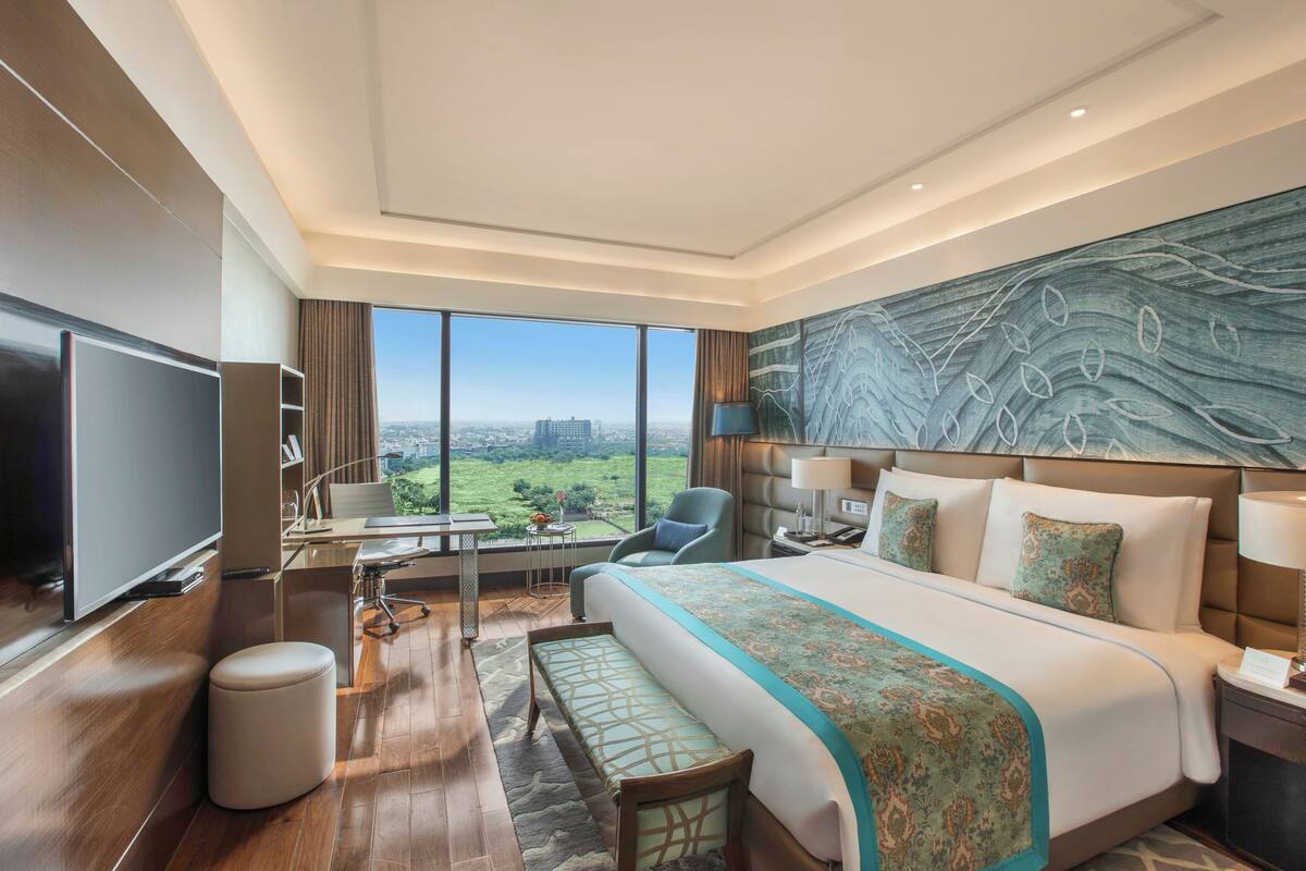 Une chambre d  ’hôtel moderne dotée d’un grand lit, d’un téléviseur à écran plat, d’un bureau avec une chaise et offrant une vue sur le paysage urbain.