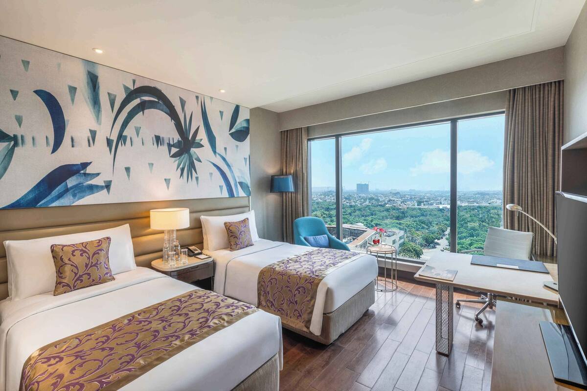 Une chambre d’hôtel avec deux lits, un bureau, une chaise et une grande fenêtre donnant sur la ville.