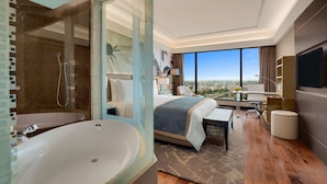 A modern hotel room with a large bathtub, a bed with a view, a desk, and a television. - The Leela Ambience Convention Hotel Delhi  (New Delhi)