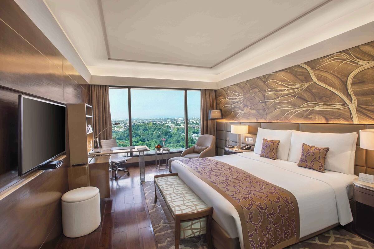 Une chambre d’hôtel moderne dotée d’un grand lit, d’une télévision à écran plat, d’un bureau avec une chaise et offrant une vue sur la ville.