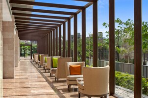 Een overdekt terras met stoelen en tafels, een betegelde vloer, en uitzicht op groen en gebouwen.
