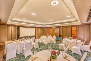 Una sala conferenze con tavoli rotondi, sedie bianche e pavimento rivestito di moquette.