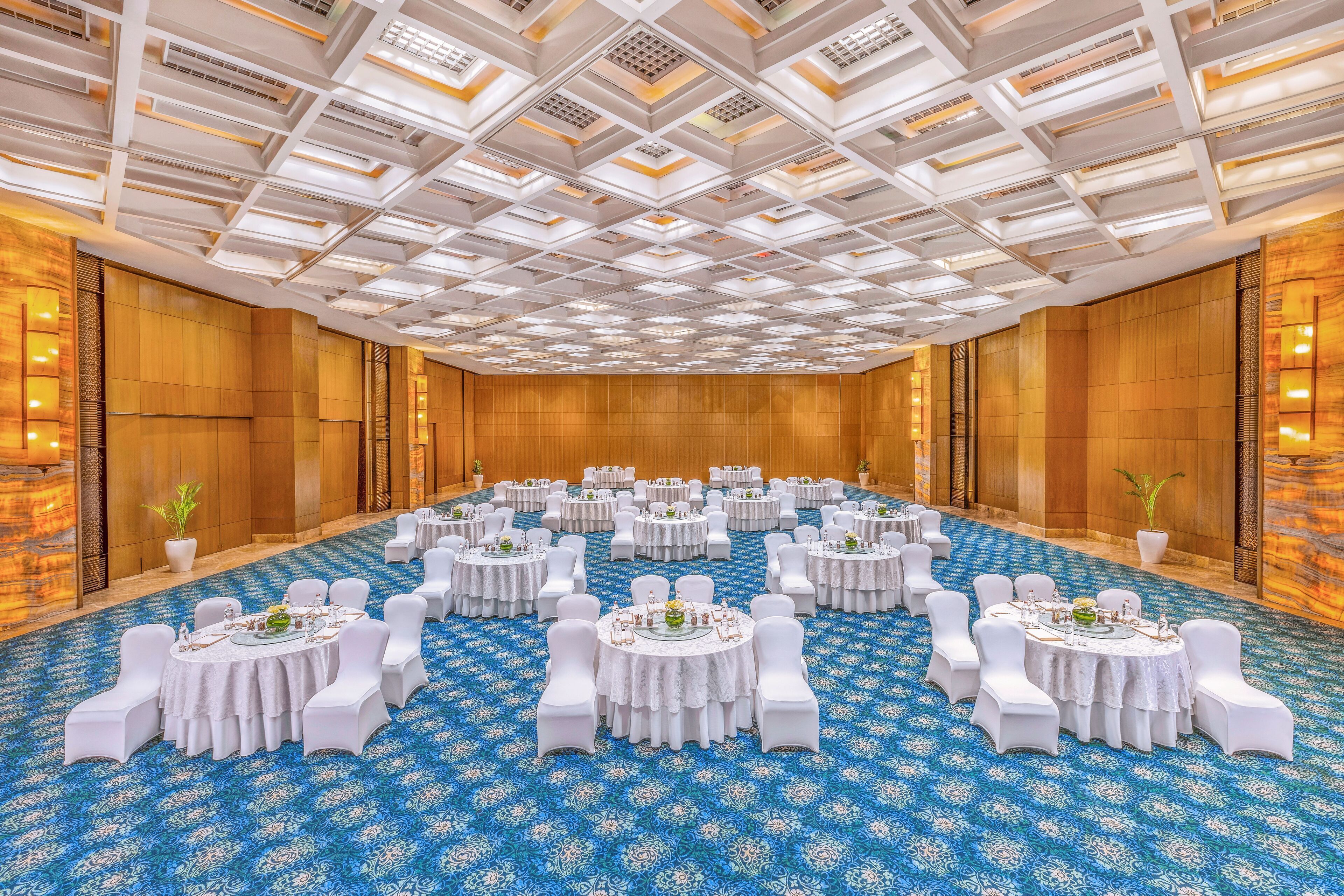 A large conference room with multiple round tables, white chairs, and a blue patterned carpet.