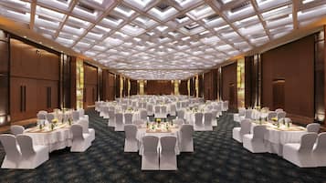 A large banquet hall with round tables, white chairs, and chandeliers.