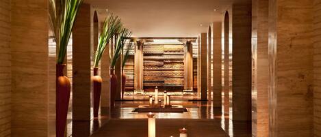 A hallway with a central water feature, flanked by tall columns and potted plants.