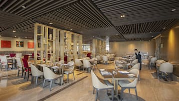 Un restaurante espacioso con decoración moderna, que cuenta con techos altos, suelos de mármol y diversas opciones de asientos.
