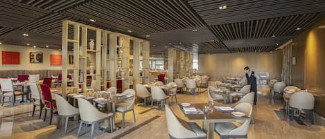 A spacious restaurant with modern decor, featuring high ceilings, marble flooring, and a variety of seating arrangements.
