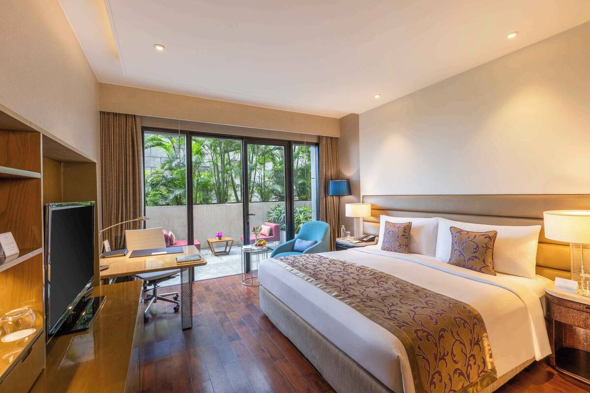 Une chambre d’hôtel avec un grand lit, un bureau avec un ordinateur, une chaise et une petite table avec une lampe.